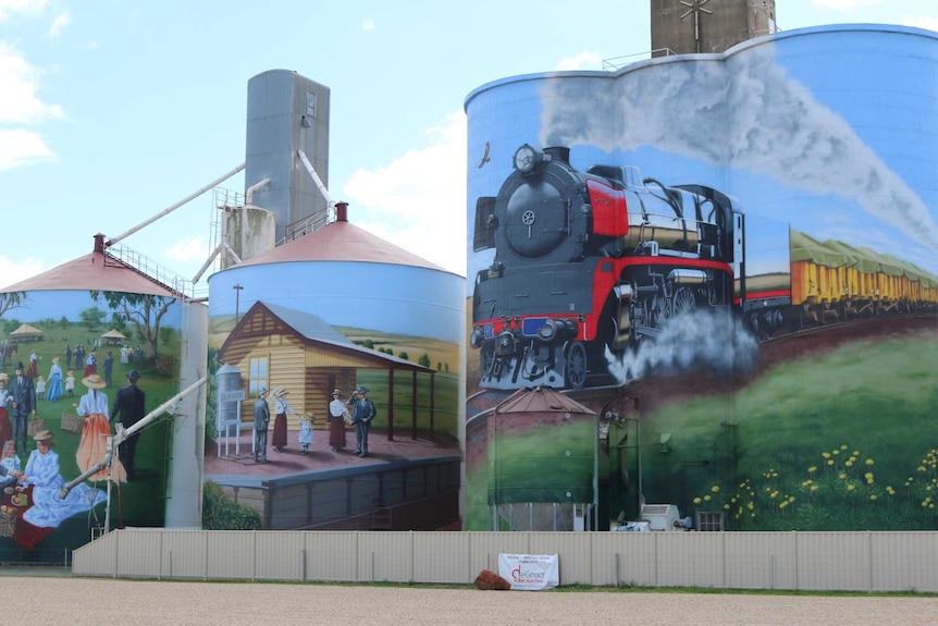 three silos with picture of train, train station and picnic painted on