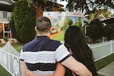 A man and woman hugging in front of a for sale sign at a house