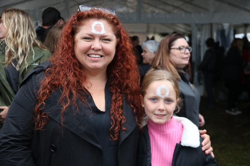 A woman puts her arm around a small child as she smiles at the camera