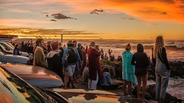 Cars and people lined up at the beach, with a sunset overhead.