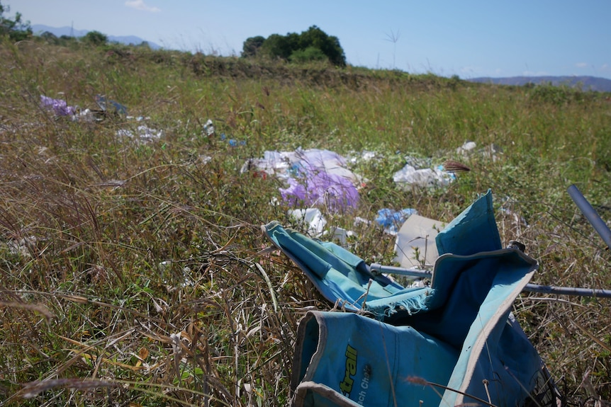 A collapsed camping chair and plastic rubbish scattered throughout grass under midday sun. 