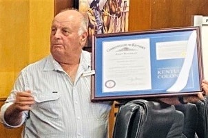 A balding man holds a framed award