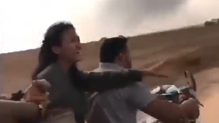 A screenshot of a video shows a woman reaching out in distress as she is driven away by men in a desert.