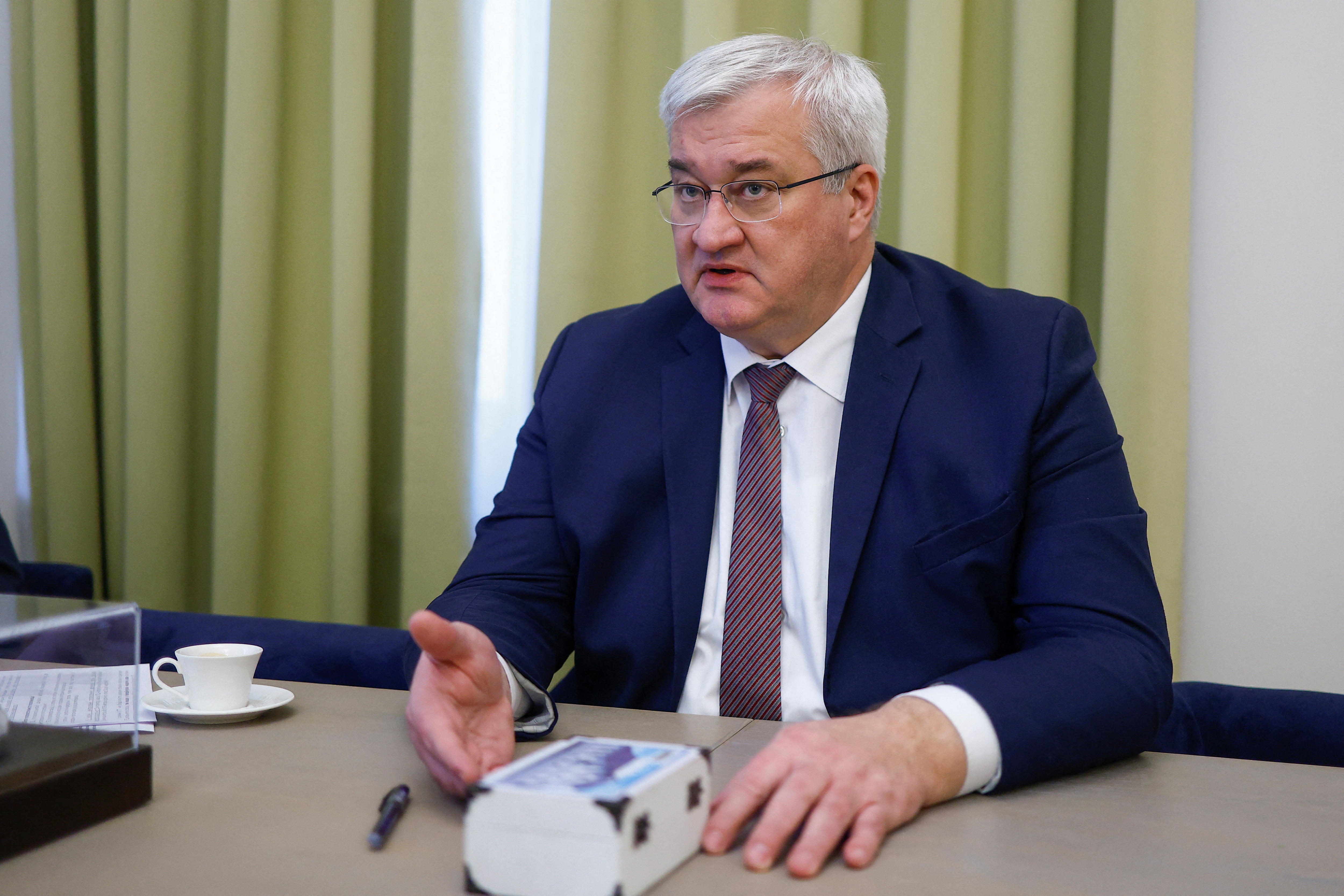 The Ukrainian foreign minister, Andrii Sybiha, sitting at a table, with a teacup next to him, with his palm open.