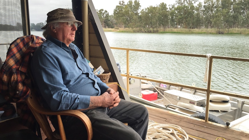 Rodney West sits on a rocking chair on the back deck of his houseboat and looks out at the river.