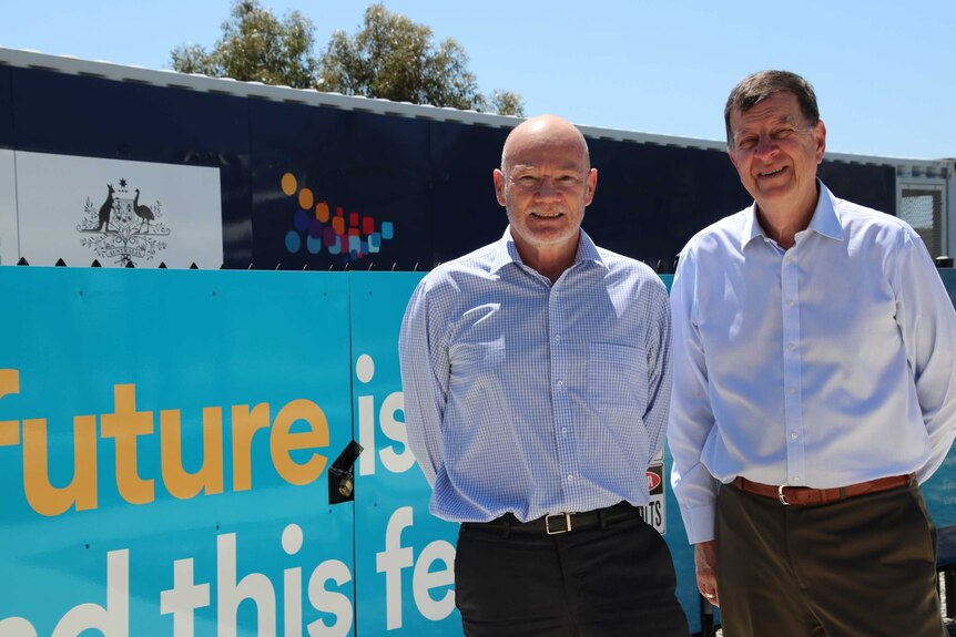 Greg Bourne and Andrew Stock stand in front of a large community battery at Alkimos Beach.