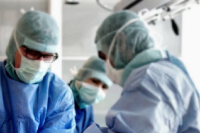 Three doctors in medical scrubs at work in a surgery.