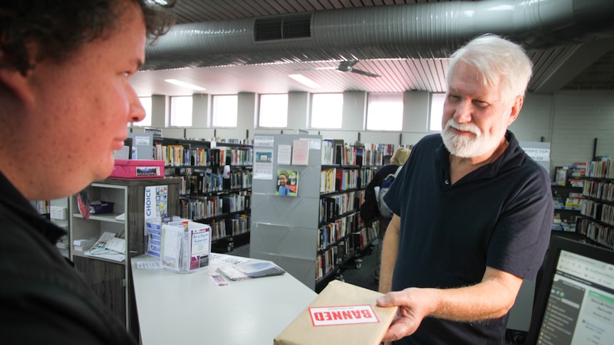 Two men stand at the library counter checking out a book