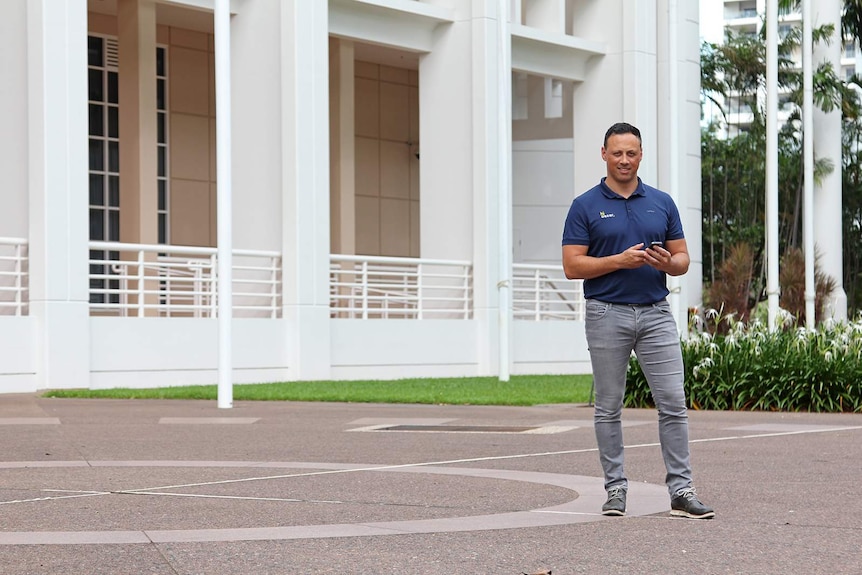 Dan Broughton stands before parliament house holding his phone.