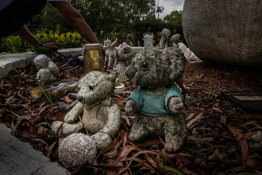 Weathered plush toys and trinkets sit among brown leaves.