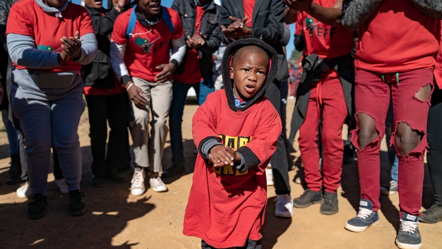 A young boy joins the crowd at an EFF rally in an oversize red t-shirt.