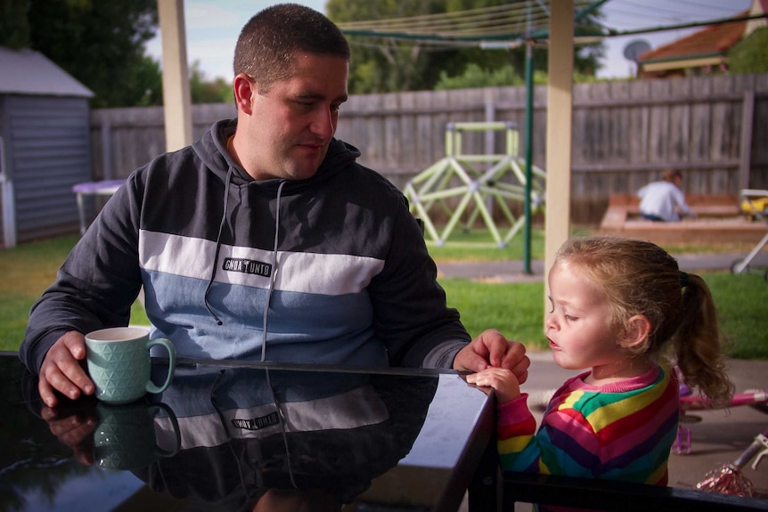 A man sits outside while a little girl stands next to him.