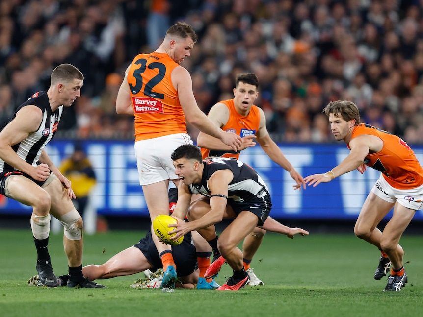 A Collingwood player bends down with his hands on the ball as he tries to burst free as three GWS defenders watch.