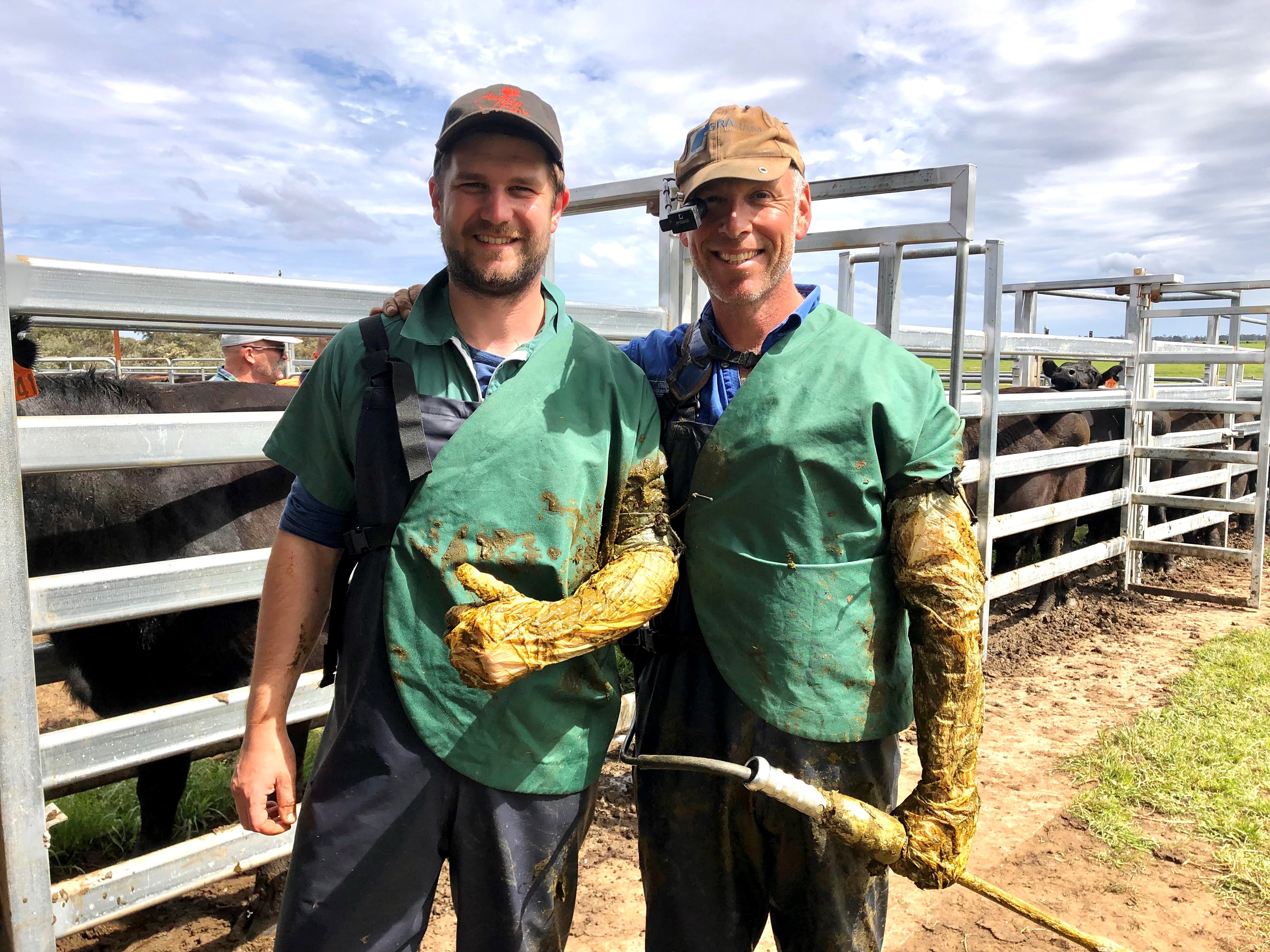 Two men in vet uniforms pose next to cattle yards
