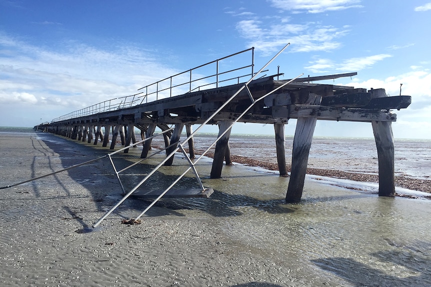 A section of wooden jetty with bent metal and stripped of wood due to storm damage.