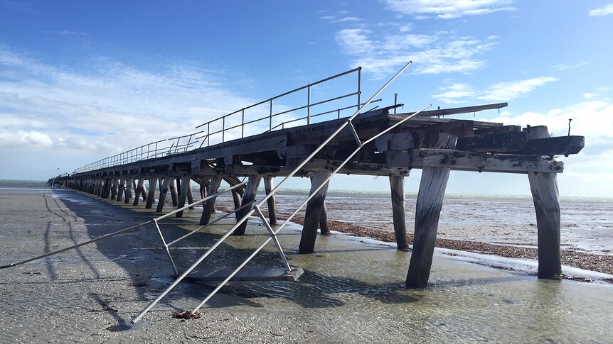 A section of wooden jetty with bent metal and stripped of wood due to storm damage.