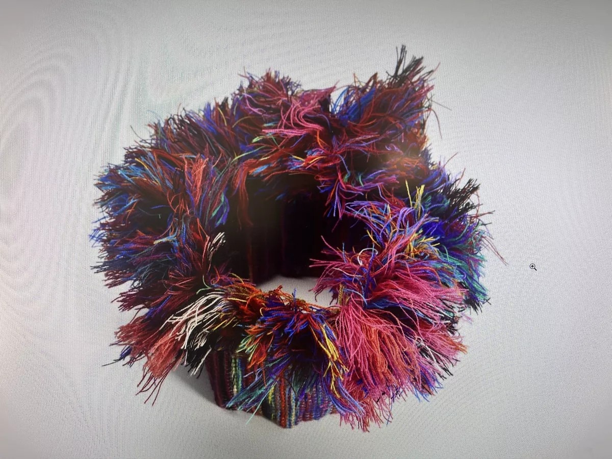 Uma peça de arte têxtil em forma de anel com muitos fios coloridos soltos saindo