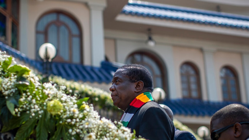 Zimbabwe's President Emmerson Mnangagwa walks up steps in front of an opulent mansion with a blue roof.