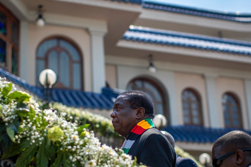 Zimbabwe's President Emmerson Mnangagwa walks up steps in front of an opulent mansion with a blue roof.