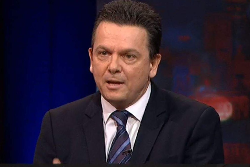 Nick Xenophon wears a dark suit and white tie, he has short dark hair.