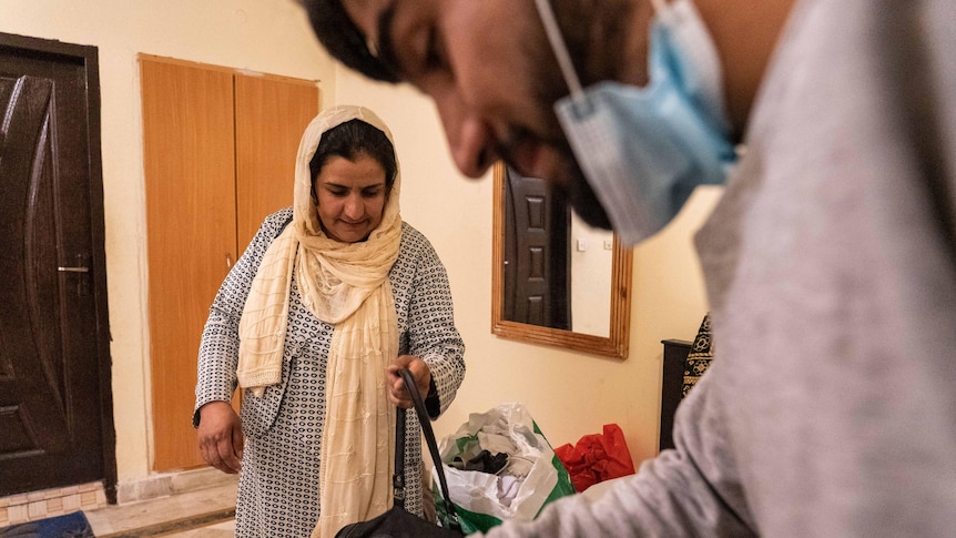 Une photo d'une femme avec un foulard lâche ramassant son sac tandis qu'un homme portant un masque l'encadre au premier plan.