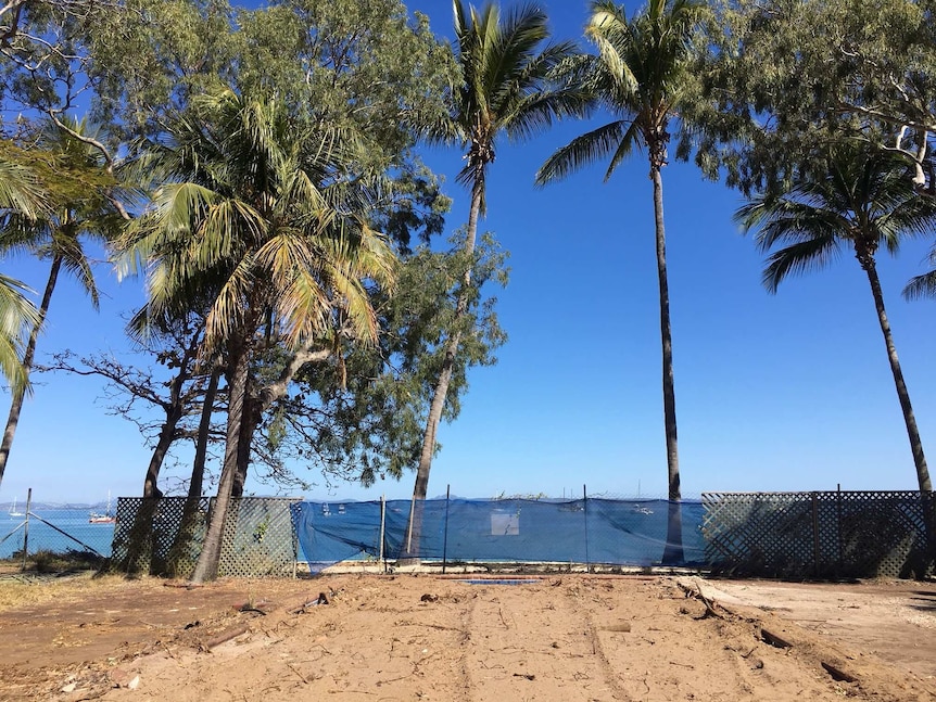 Sand covers a pool, blue sky with palm trees in the background.