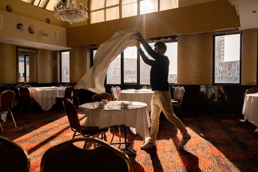 a man holding a table cloth about to place on a table
