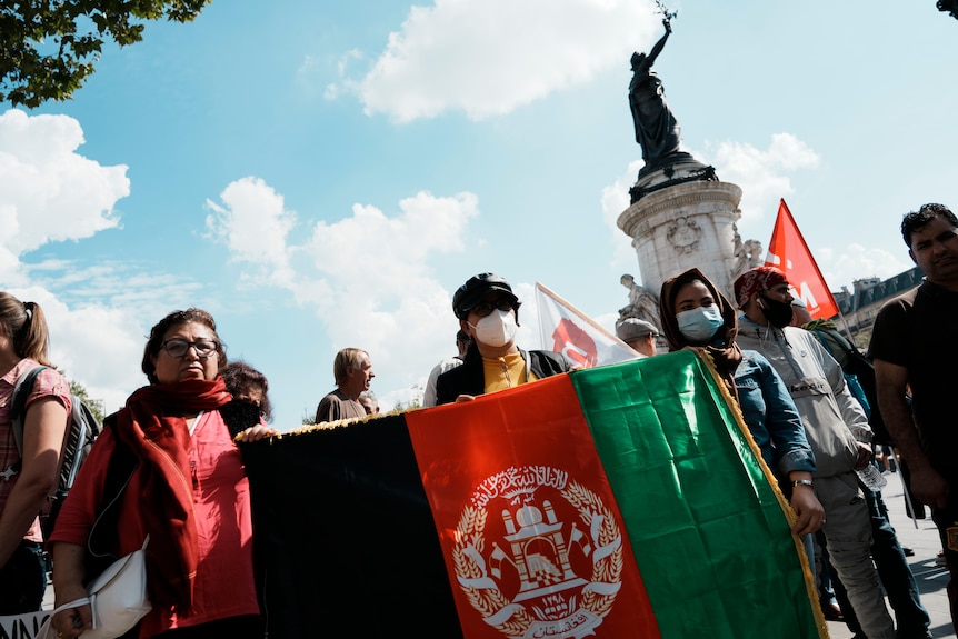 Women hold a flag of Afghanistan during a gathering in Paris