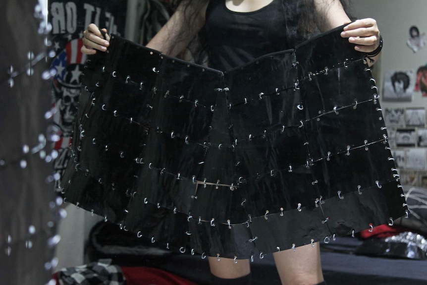 Storm Delaney holds up the skirt she designed and constructed before a mirror.