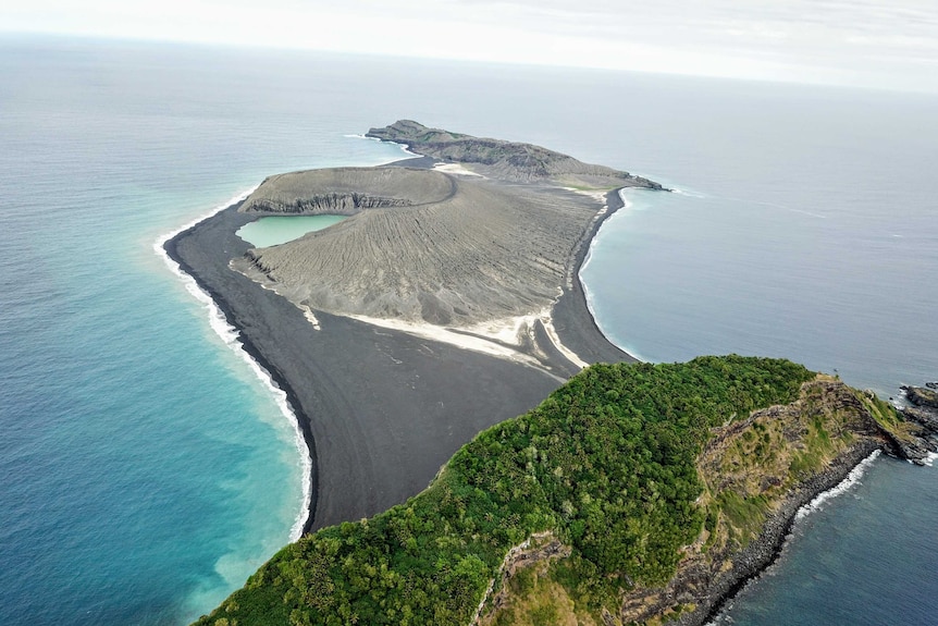 A grey volcanic island pictured from above and connected by an isthmus to an older island covered in vegetation