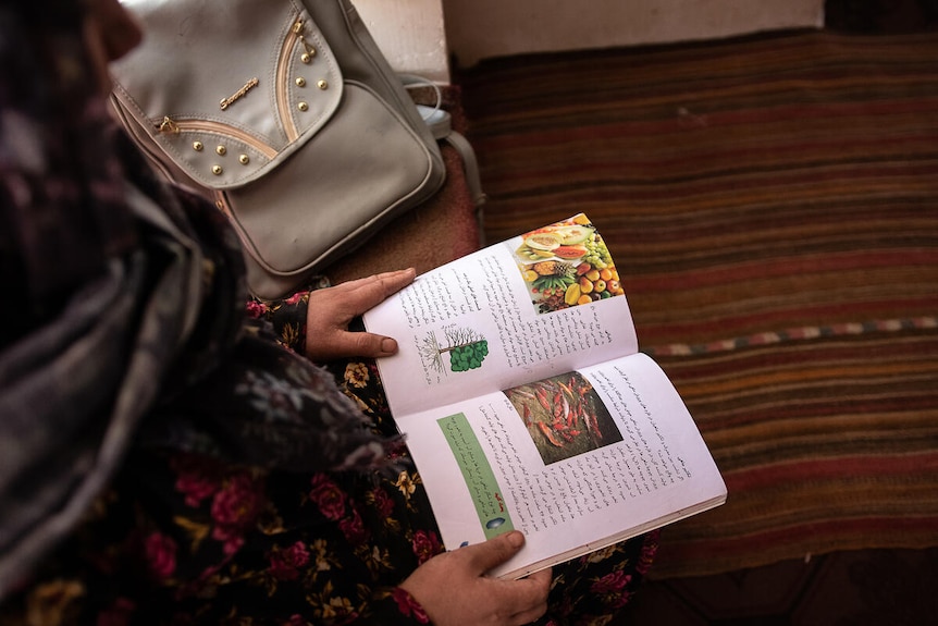Image of an open book on the lap of a girl wearing a dark floral dress and hijab