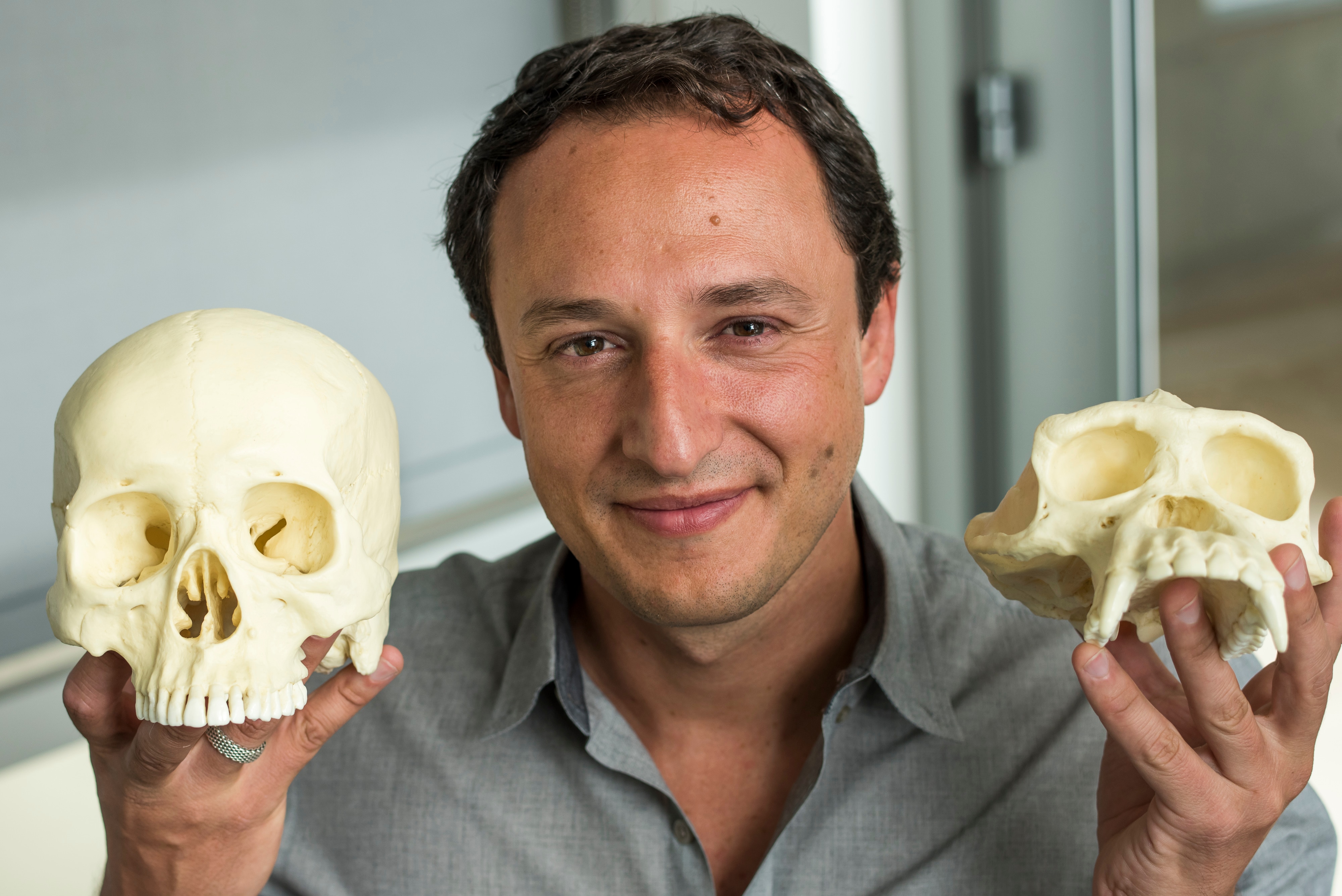 A man holds two casts of skulls in each hand and smiles at the camera
