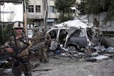 Afghan security personnel (L) keeps watch next to a damaged car belonging to foreigners, after a bomb blast in Kabul