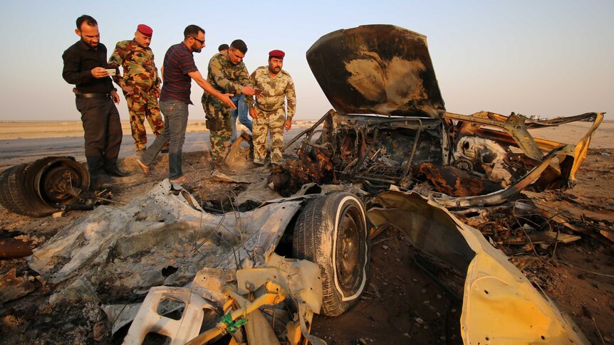 Iraqi security forces inspect the site of a bomb attack at a police checkpoint.