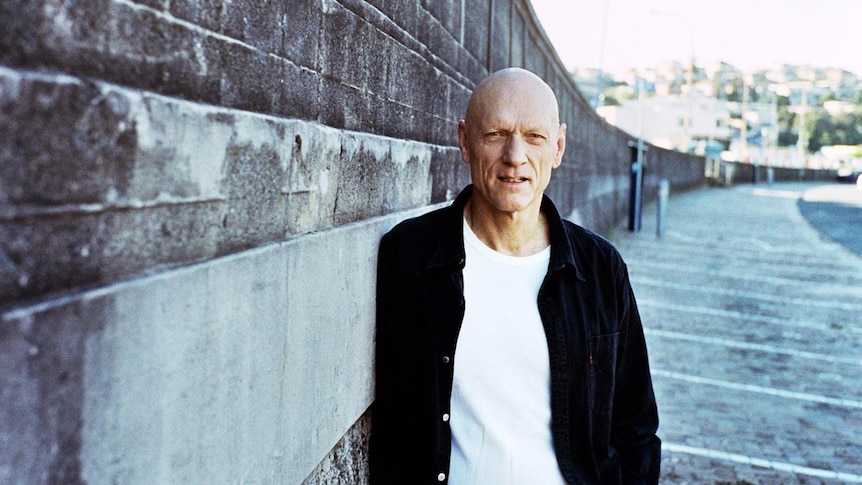 Midnight Oil frontman Peter Garrett stands on an empty street in front of a brick wall