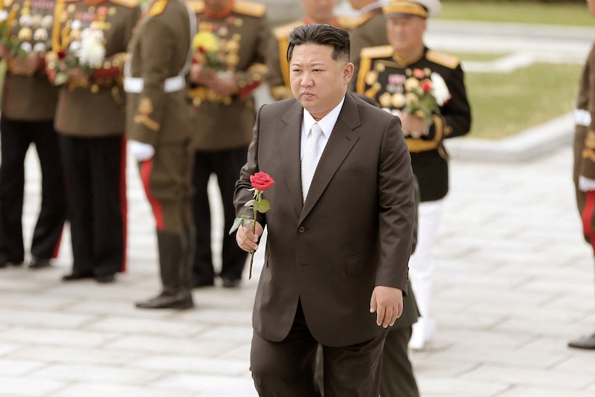 Kim Jong Un holds a red flower in suit. 