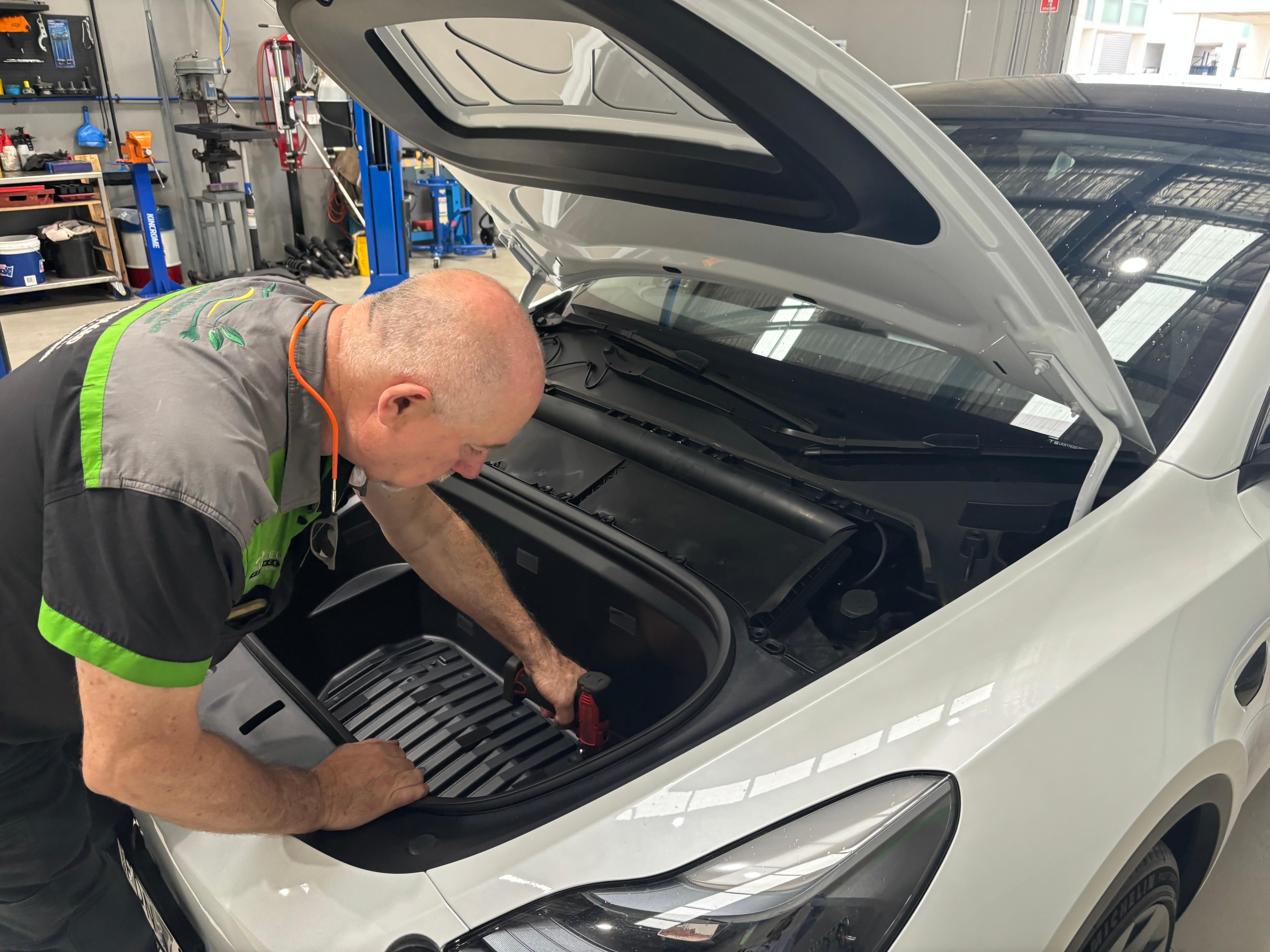 A man looks under the bonnet of a car inside a mechanics shop. 