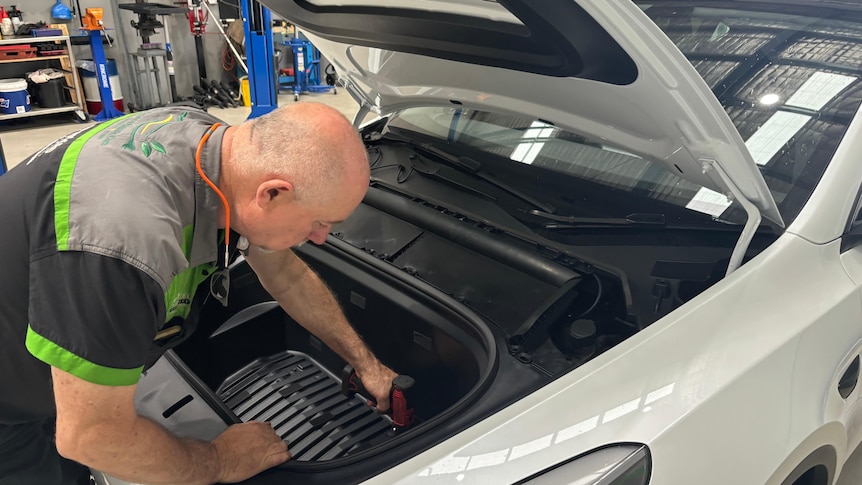 A man looks under the bonnet of a car inside a mechanics shop. 