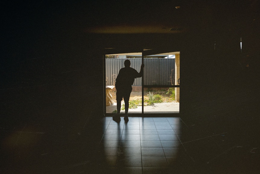 Dan in silhouette stands in the doorway of his house looking outside