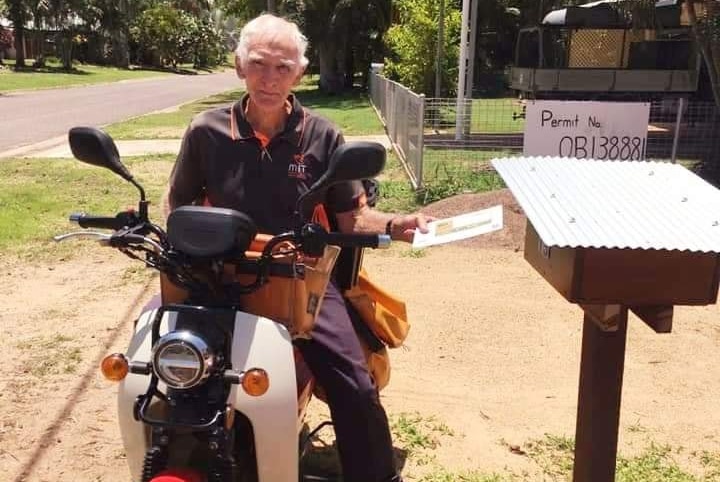 man sits on bike holding envelope in front of mail box