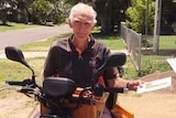 man sits on bike holding envelope in front of mail box