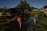 Young girl walks wades through floodwaters, with submerged homes in the background.