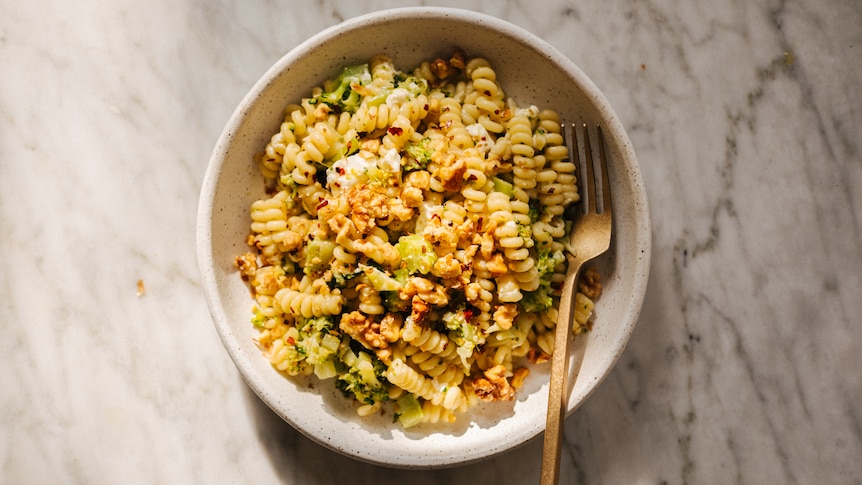 A bowl of fusilli pasta cooked with chopped broccoli, garlic and topped with feta, chilli flakes, walnuts.