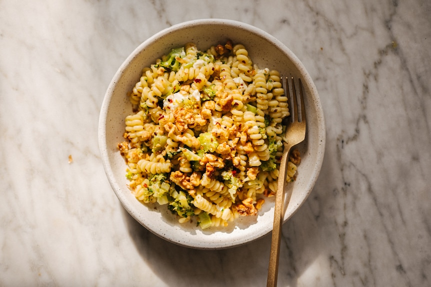 A bowl of fusilli pasta cooked with chopped broccoli, garlic and topped with feta, chilli flakes, walnuts.