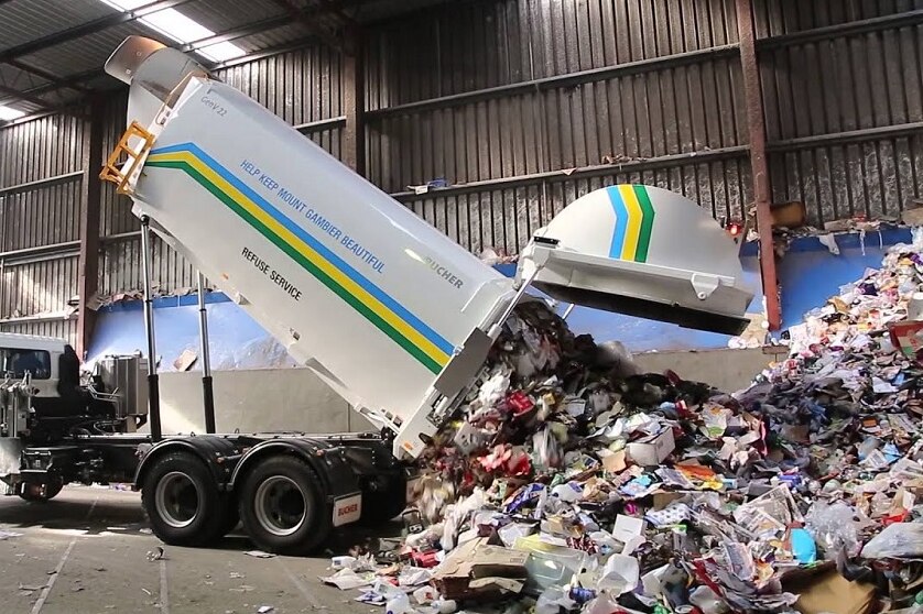A garbage truck elevates its load to dump recyclables on the ground.