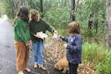 A woman, her children, and a dog stand on a bush road.