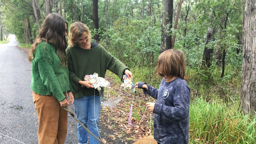 A woman, her children, and a dog stand on a bush road.