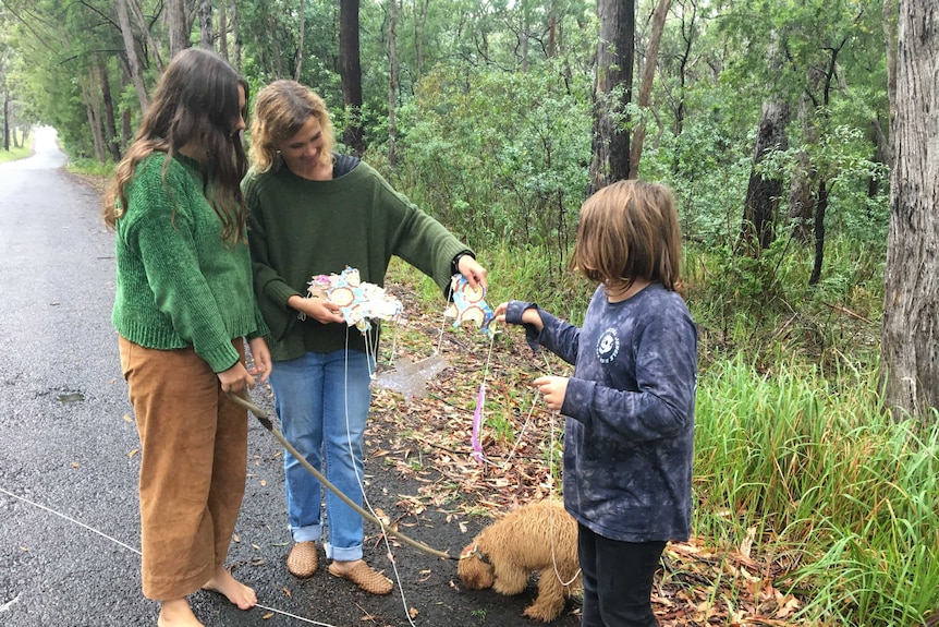 A woman, her children, and a dog stand on a bush road.