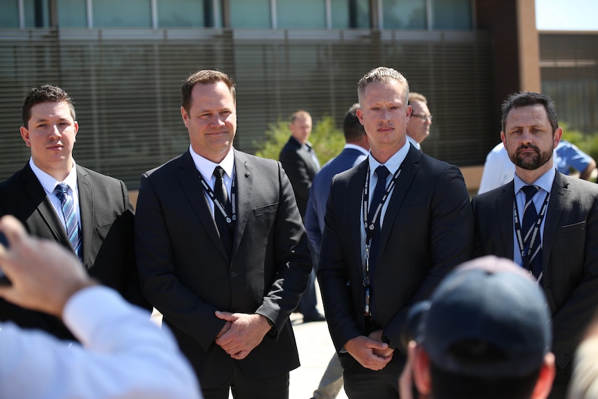 Four police in suits stand together at a press conference