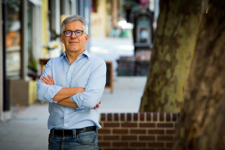 Gordon Renouf stands in a street with his arms folded, wearing a blue shirt.